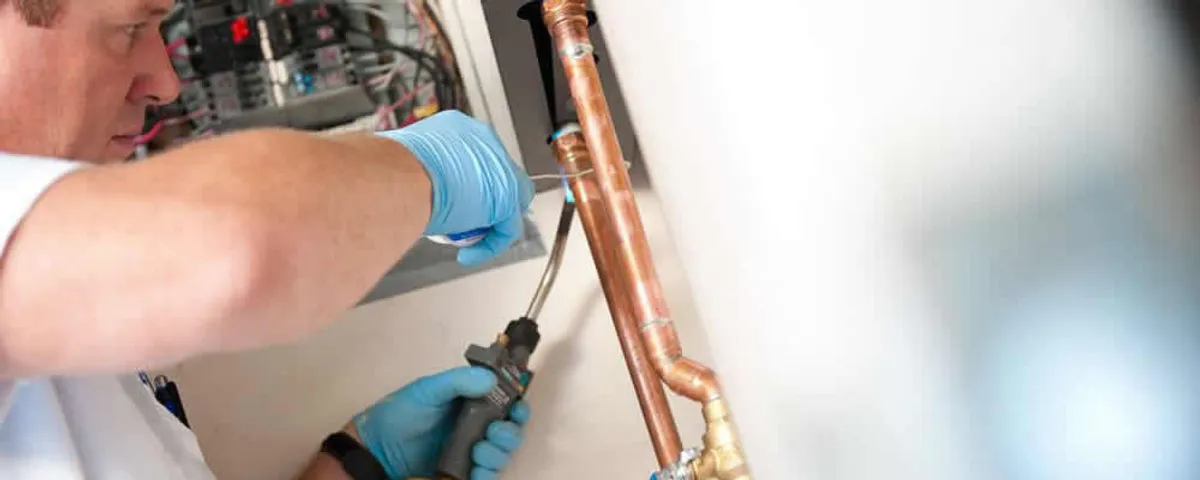 Water heater repair technician testing copper pipe connections and controls in Bloomington, IN